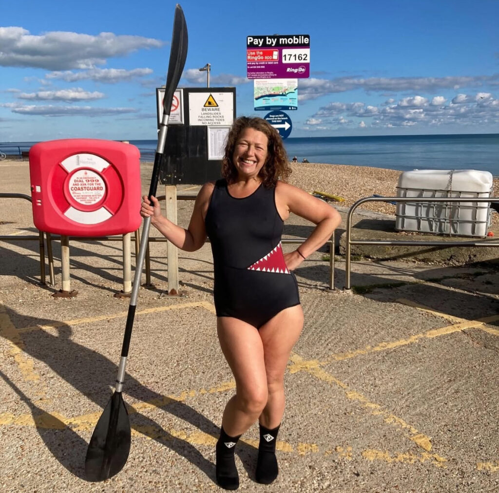 A woman in a swimming costume holding an ore on the beach